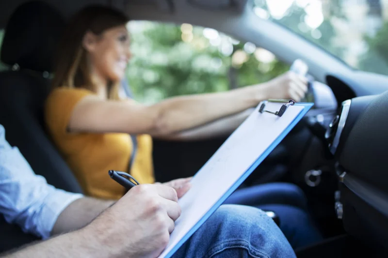 close up view driving instructor holding checklist while background female student steering driving car scaled 1 e1675289890288